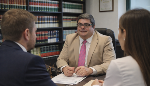 Abogado mercantil reunido con clientes en despacho con librería jurídica asesorando sobre problemas de empresa