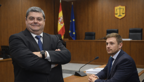 Abogado mercantil en juzgado asesorando a cliente antes de juicio con toga española