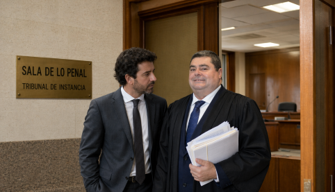 Letrado Juan Madrid Salinas con toga española y documentos en mano junto a cliente en pasillo de la Sala de lo Penal del Tribunal de Instancia
